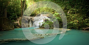 Waterfall in forest with sunlight beams and rays through trees