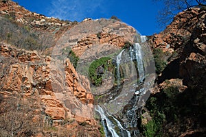 WATERFALL AND GREEN VEGETATION AGAINST SHEER ROCK