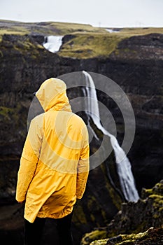 Waterfall Haifoss in Iceland. A young guy stands on a cliff and looks at the waterfall.