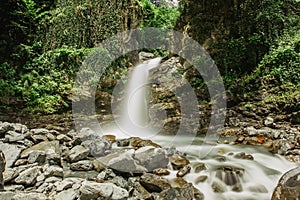 Waterfall hidden in the jungle. Flowing water. Stream in the mountains. Tropical nature. Rocks, river and trees. Long exposure