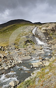 Waterfall lighted by sunlight in dramatic scene and dark clouds rolling in