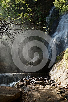 Waterfall and lower cascade in the forest with water fog lit wit