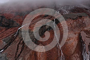 A waterfall of meltwater coming from a gletser from the chimborazo surrounded by rocks with a red grey and black coloration