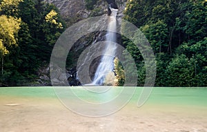 Waterfall in midst of forest landscape cascading into a clorful turquopise and brown pond