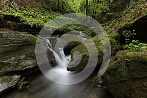 A waterfall in the midst of a magical wild nature, rocks covered with moss and forest around.