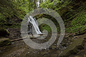 A waterfall in the midst of a magical wild nature, rocks covered with moss and forest around.