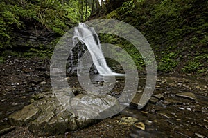 A waterfall in the midst of a magical wild nature, rocks covered with moss and forest around.