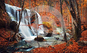 Waterfall at mountain river in autumn forest at sunset.