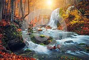 Waterfall at mountain river in autumn forest at sunset.
