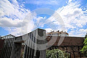 A waterfall over a stone wall with a doorway on a curved footpath in the garden with blue sky and powerful clouds