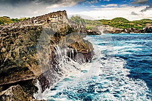 Waterfall into the sea. Waves splashing against a cliff. Blue water. Angel billabong, Nusa Penida, Bali