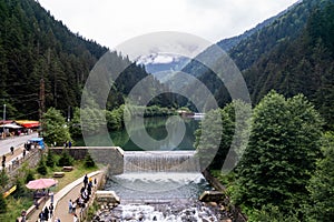 Waterfall on the Sera lake on a gloomy day with forested mountains and cloudy sky in the background