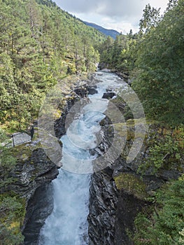 Waterfall Slettafossen at Verma with deep narrow Rauma river canyon at Romsdalen valley with rocks and green forest. Blue sky photo