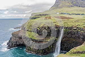 Waterfall and a small village set against the backdrop of beautiful mountains and dramatic clouds. Faroe islands