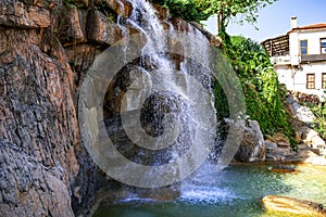 Waterfall from a stone cliff close-up. Falling and splashing streams of water against the background of a modern building on a