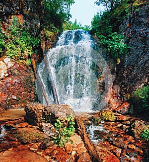 Waterfall among stones and taiga driftwood in water and wet stones