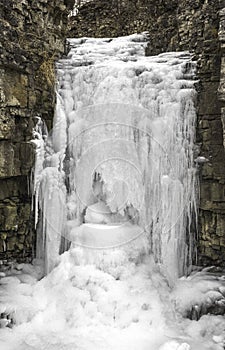 Waterfall and stream frozen by winter cold as it cut through lay