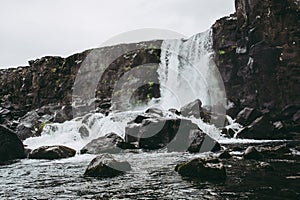 The waterfall of in Thingvellir National Park, Iceland flowing from the river into the pool filled with rocks