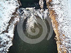 Waterfall on winter creek. Snow on frozen riverbanks. Top Aerial View Of River Cascade. Stream water flowing between rocks