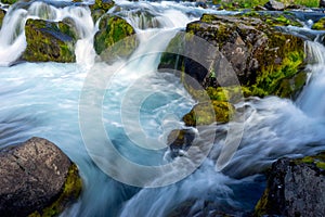 Waterfalls with clear blue water and green mossy boulders outdoors in the icelandic nature