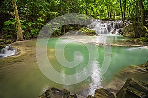Waterfalls and fish swim in the emerald blue water in Erawan National Park. Erawan Waterfall is a beautiful natural rock waterfall