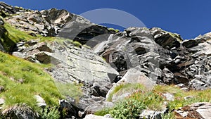 Waterfalls flowing in idyllic uncontaminated environment crossing green meadows and boulders on the Alps in summer. Slow motion, z