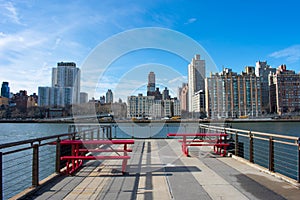 Waterfront along the East River at Roosevelt Island with Red Picnic Tables and looking towards the Upper East Side Skyline of New