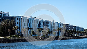Waterfront apartment condominiums in suburban community on riverbank  with tree lined walkway, blue sky in background