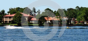 Waterfront homes on the lake with boat and kids riding a towable