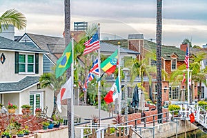 Waterfront houses colorful flags and palm trees along a canal under cloudy sky