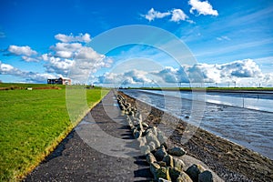 Waterfront of Husum with meadow on the left and sea on the right, beautiful clouds and wind turbines in the background, wide angle