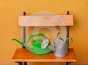 A watering can of aluminium and a plastic one laid on wooden be