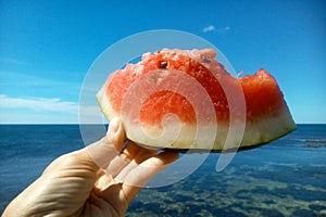 Watermellon in hand on a sea shore blue background