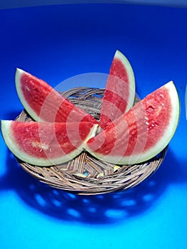  of Watermelon fruit four slince with red white and green on a brown plate in a room with blue color Background