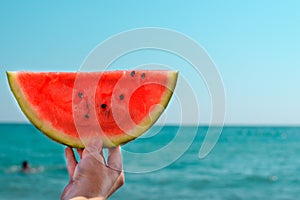 Watermelon, juicy, red slice in the hands of woman against the background of the ocean.