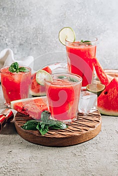 Watermelon lemonade with lime and fresh basil leaves on concrete background. Refreshing summer drink