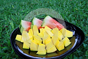 Watermelon and mango on a black plate in the grass