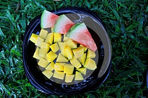 Watermelon and mango on a black plate in the grass