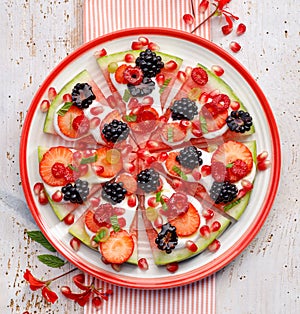 Watermelon pizza, vegetarian, fruit  pizza with creamy natural yogurt and fresh fruits  on a plate, on a white wooden table, top v