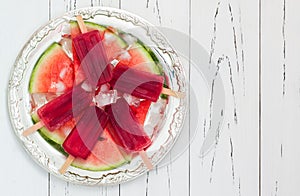 Watermelon popsicles - ice pops - on slices of ripe juicy watermelon, served on vintage silver tray over old rustic wooden table