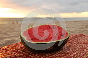 A watermelon on the sandy beach on the sunset.