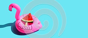 Watermelon slice popsicle with inflatable of pink flamingo on blue background. Summer background