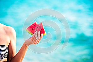 Watermelon slice in woman hand over sea - POV. Summer beach concept. Tropical fruit diet.