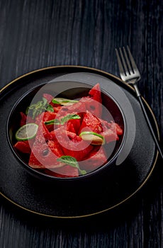 Fresh watermelon salad kept in a black bowl and plate on dark background