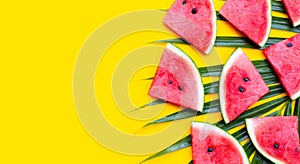 Watermelon slices on tropical palm leaves on yellow background.