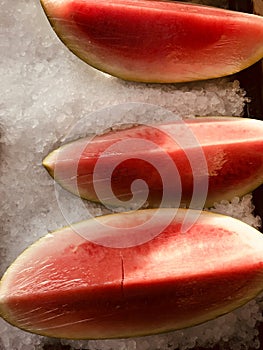 Watermelon slices are wrapped in plastic and sit on ice in the midday sun
