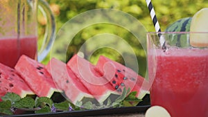 Watermelon smoothie in a glass with melon slices in background