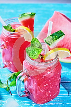 Watermelon summer cocktail with ice and mint leaves. Cold refreshment drink on blue wooden background with copy space.