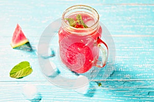 Watermelon summer cocktail with ice and mint leaves. Cold refreshment drink on blue wooden background with copy space.