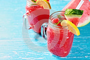 Watermelon summer cocktail with ice and mint leaves. Cold refreshment drink on pastel blue wooden background.